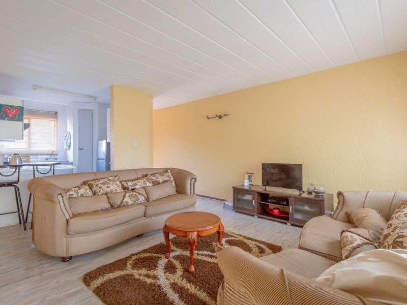 An open-plan living area featuring laminate flooring, textured walls, and a panelled ceiling, with an adjacent kitchen area visible in the background.