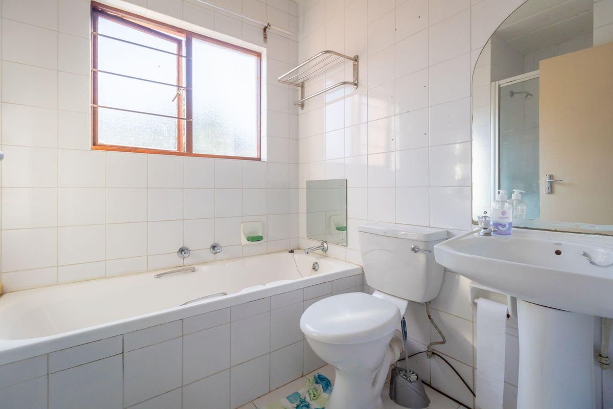 A functional bathroom featuring a bathtub, pedestal sink, toilet, and tiled finishes, offering potential for modernization and cosmetic updates.