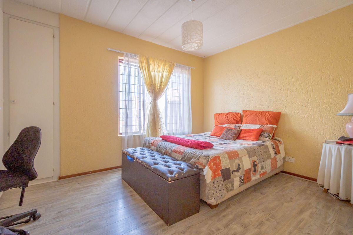 A bedroom featuring laminate flooring, a built-in cupboard, and security bars on the window, with textured yellow walls.