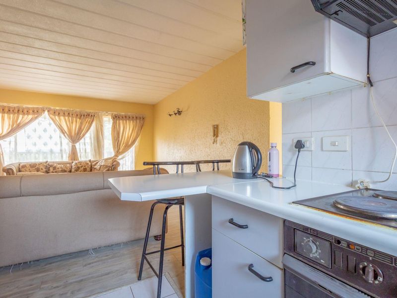 Open-plan kitchen and living area featuring a breakfast bar, built-in oven, and hob, with a functional layout connecting the cooking and lounge spaces.