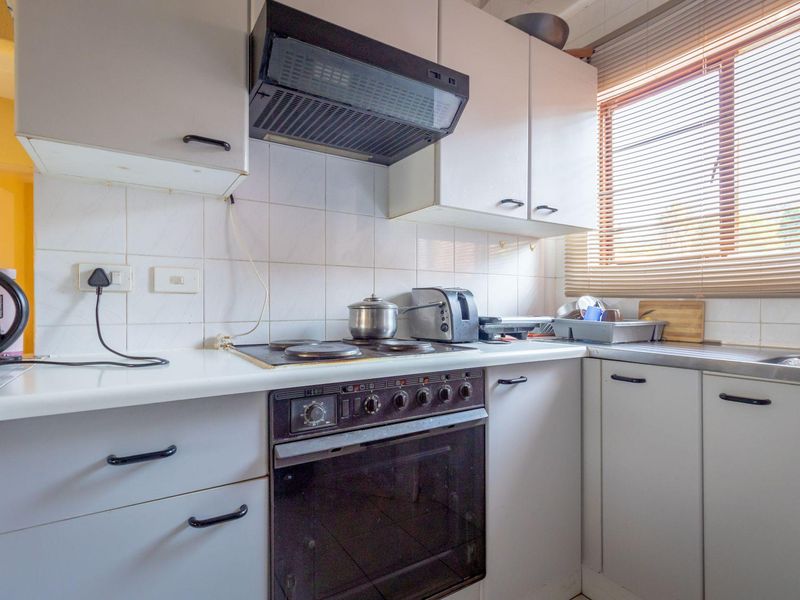 A functional kitchen featuring built-in cabinetry, an integrated oven and hob, extractor fan, and a stainless steel sink with natural light from the window.