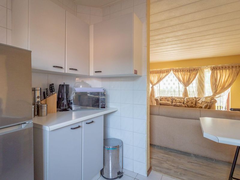 A compact kitchen area featuring white built-in cabinetry, tiled splashbacks, and laminate countertops, with an open-plan flow into the adjacent living space.