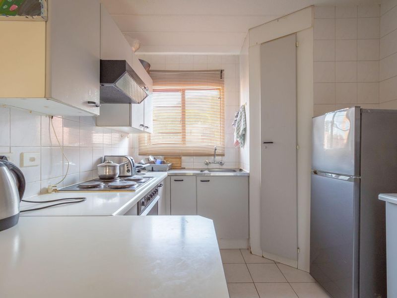 A functional kitchen featuring built-in cabinetry, an electric hob with extractor fan, tiled backsplash, and a convenient built-in pantry cupboard.