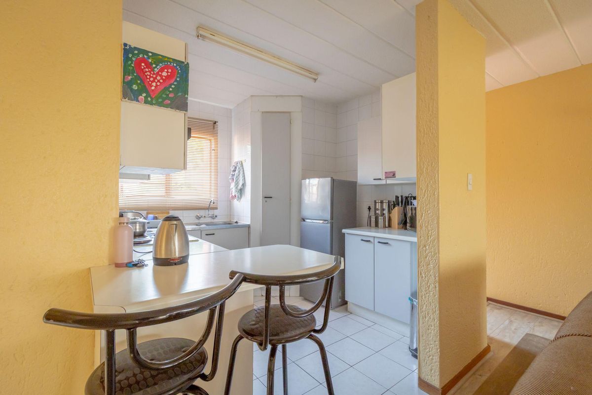 A compact kitchen featuring dated cabinetry, tiled backsplash, and tiled flooring, offering a functional layout with a breakfast bar area.
