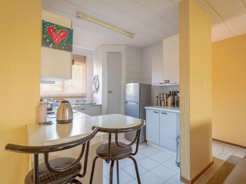 A compact kitchen featuring dated cabinetry, tiled backsplash, and tiled flooring, offering a functional layout with a breakfast bar area.