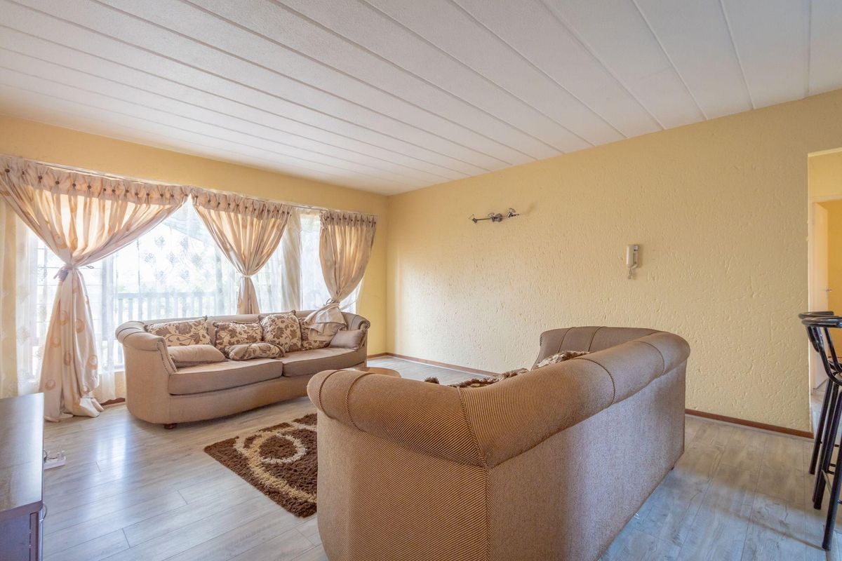 A spacious living room featuring light-toned laminate flooring, textured walls, and a large window that allows for ample natural light.