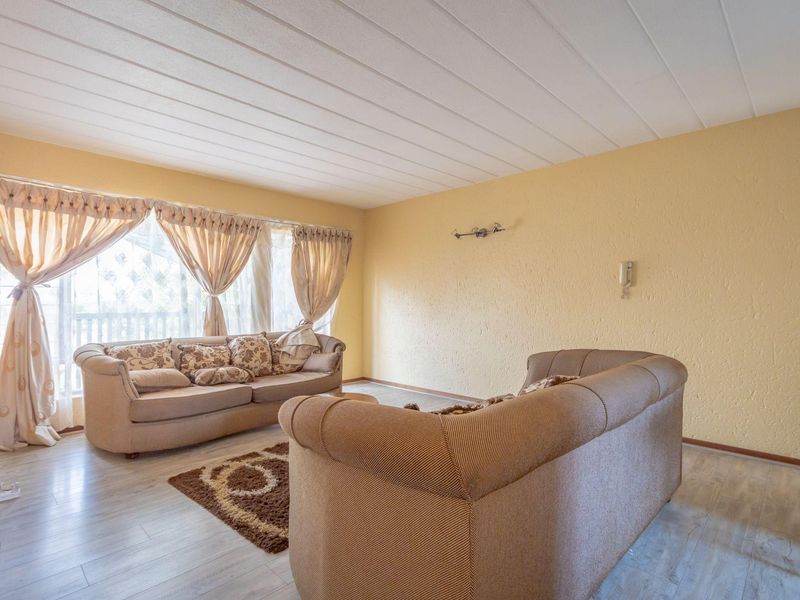 A spacious living room featuring light-toned laminate flooring, textured walls, and a large window that allows for ample natural light.