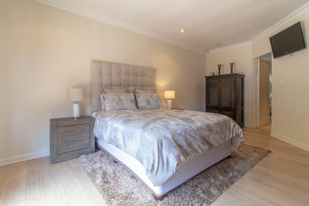 A well-maintained bedroom featuring light-toned laminate flooring, crown molding, and a neutral color palette, providing a comfortable and inviting living space.