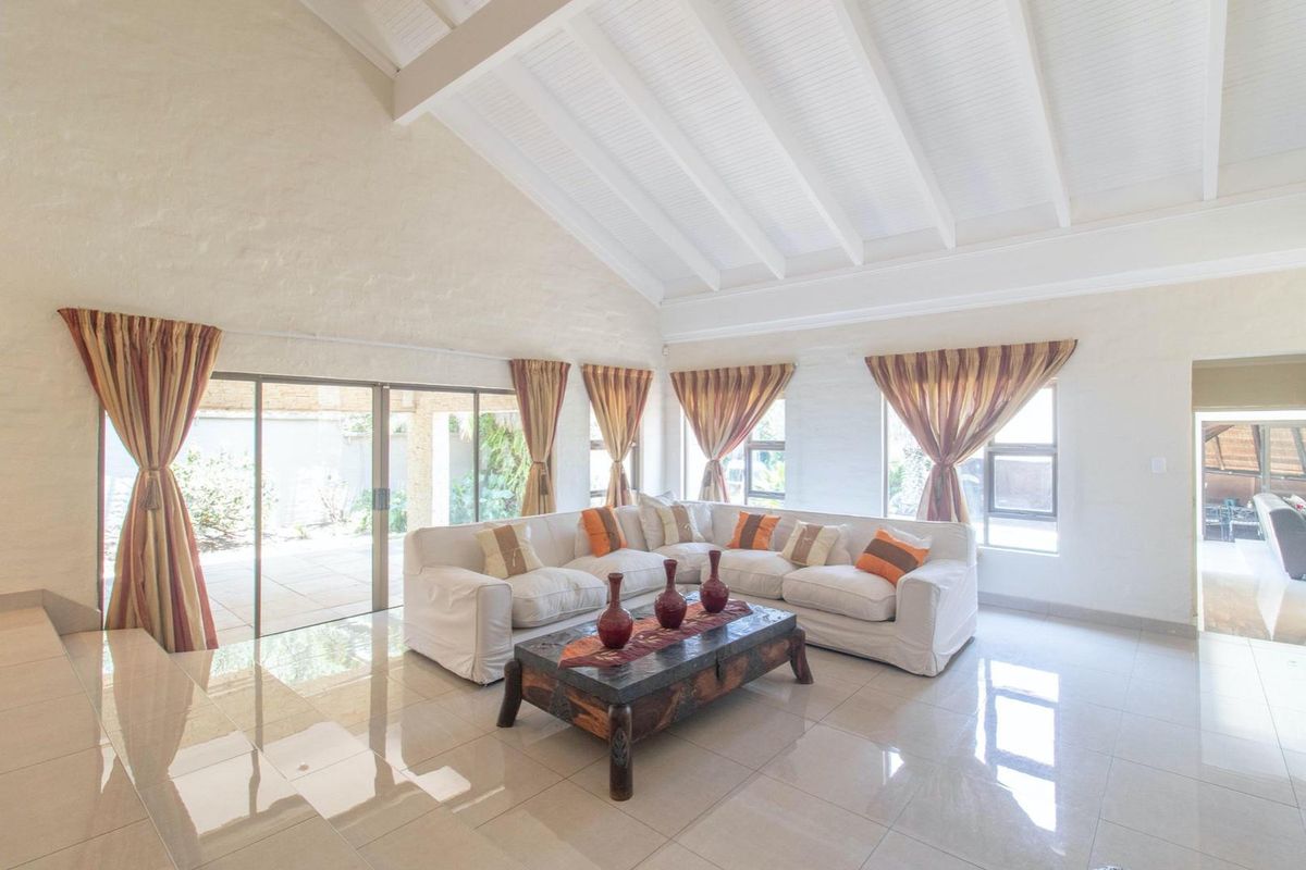 Spacious living room featuring high vaulted ceilings with exposed beams, large tiled flooring, and expansive sliding glass doors providing access to the outdoor patio area.
