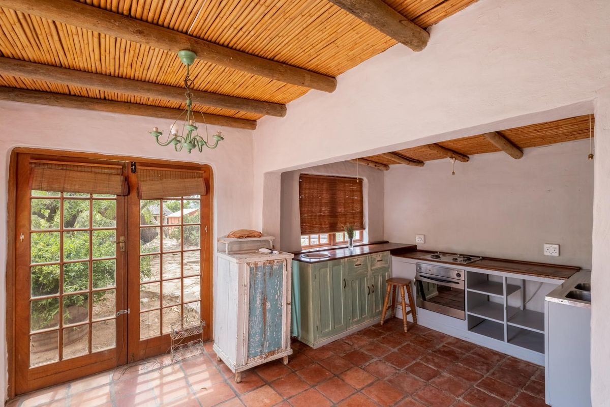Rustic kitchen featuring terracotta floor tiles, exposed beam and bamboo ceiling, built-in cabinetry, integrated oven, and direct access to the garden through wooden doors.