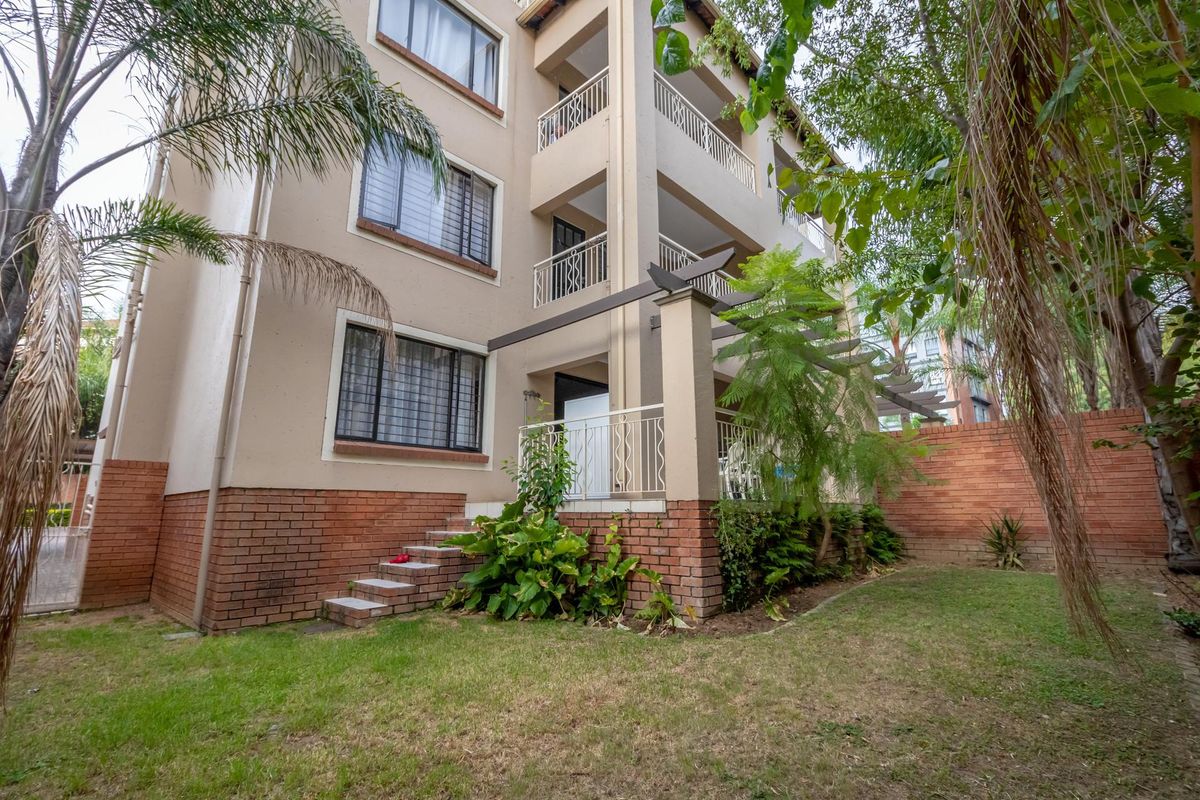 Exterior view of a multi-story apartment building featuring a ground-floor patio, brick base detailing, and a small private garden area.