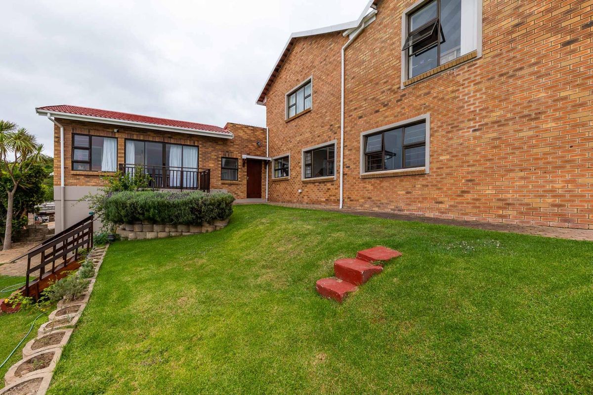 Rear view of a multi-level brick house featuring a landscaped lawn, raised garden bed, and external staircase leading to the upper level.