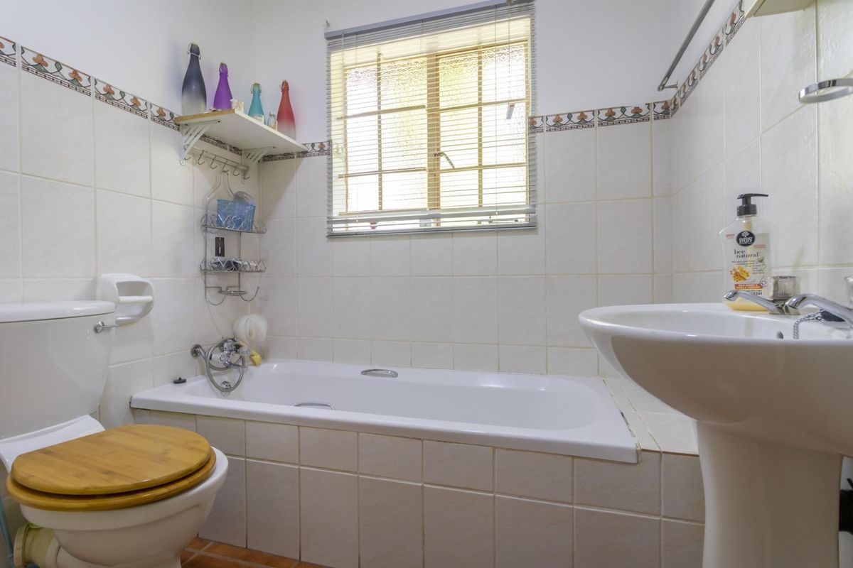 A functional bathroom featuring a built-in bathtub, pedestal basin, and toilet, finished with classic wall tiling and a window for natural light.