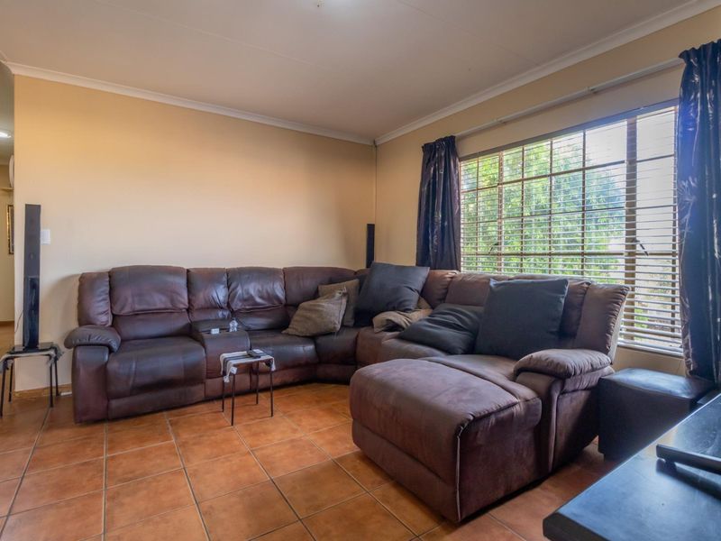 A living room featuring ceramic floor tiles, coved ceiling cornices, and large windows with fitted blinds, offering a functional and lived-in space.