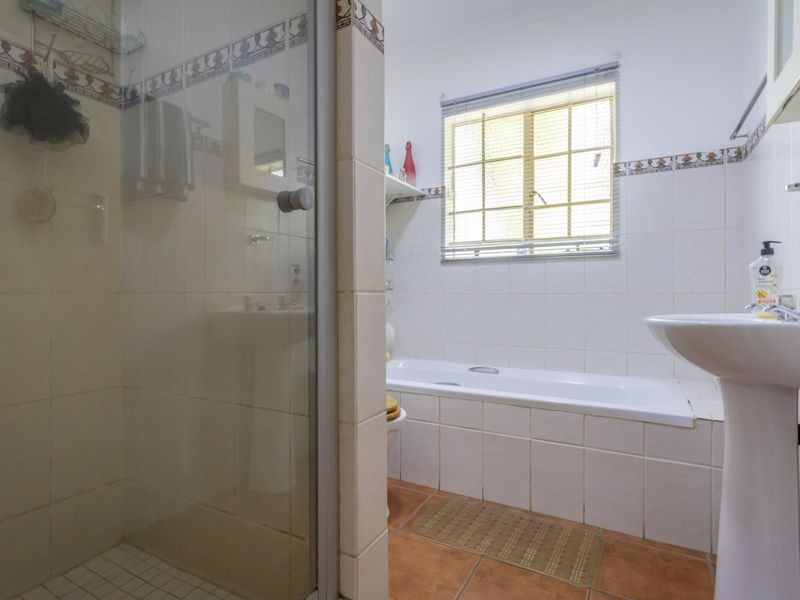 A functional bathroom featuring a pedestal basin, a built-in bathtub, and a separate glass-enclosed shower with tiled finishes.