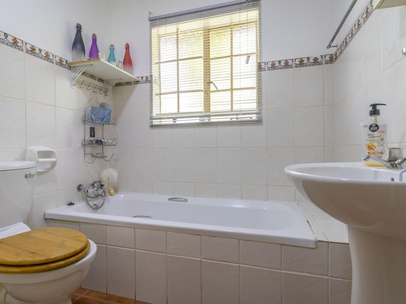 A functional bathroom featuring a built-in bathtub, pedestal basin, and toilet, finished with neutral wall tiles and a decorative border.