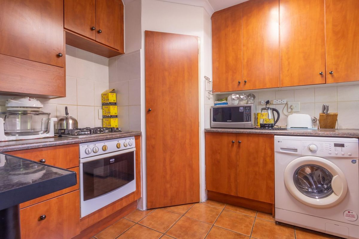 A functional kitchen featuring wood-finish cabinetry, a gas hob, built-in oven, tiled backsplash, and dedicated space for a washing machine.