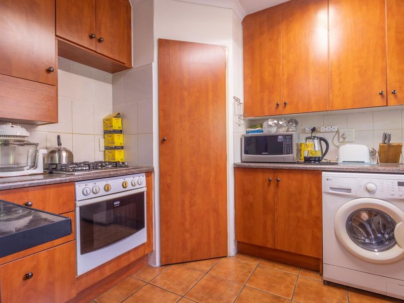 A functional kitchen featuring wood-finish cabinetry, a gas hob, built-in oven, tiled backsplash, and dedicated space for a washing machine.