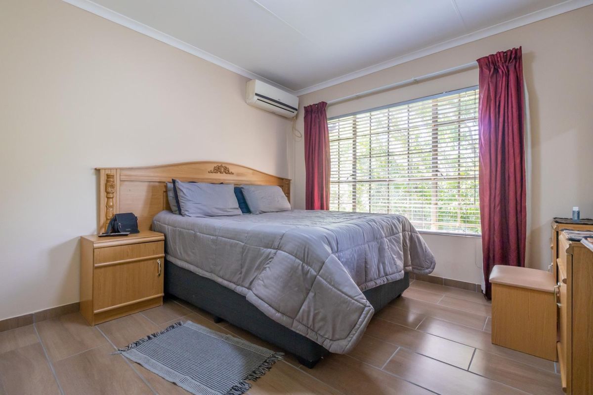 A well-maintained bedroom featuring tiled flooring, an integrated air conditioning unit, and large windows with venetian blinds for natural light control.