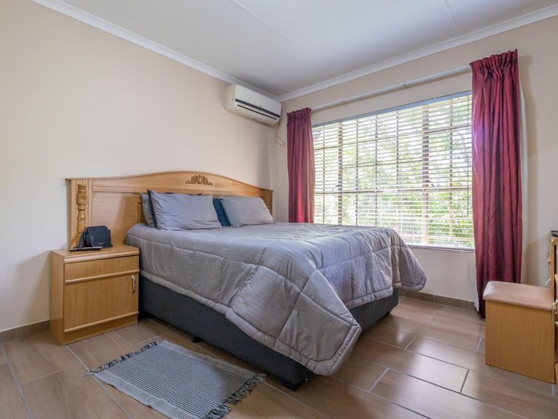 A well-maintained bedroom featuring tiled flooring, an integrated air conditioning unit, and large windows with venetian blinds for natural light control.