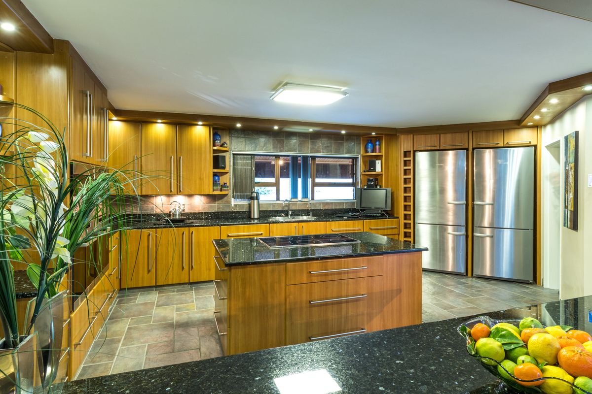 Spacious kitchen featuring warm wood cabinetry, granite countertops, a central island with a built-in cooktop, and dual stainless steel refrigerators.
