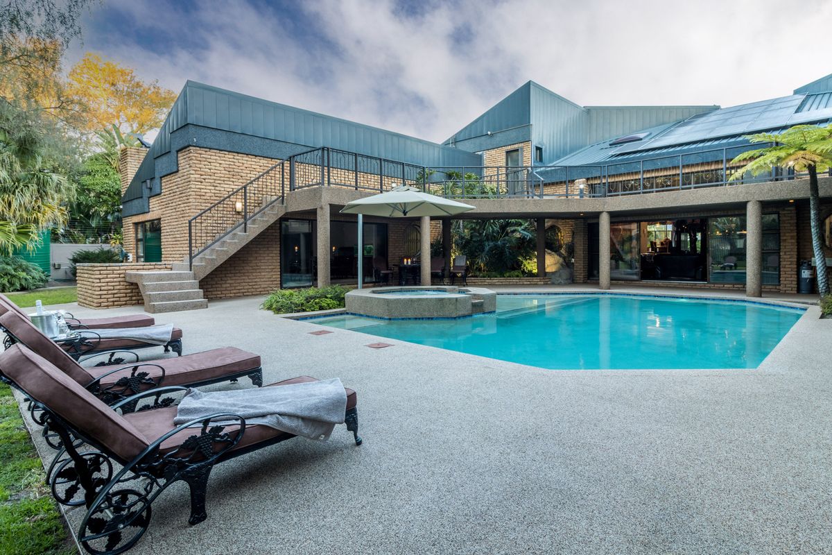 Spacious rear exterior featuring a swimming pool, integrated spa, paved patio area, and an external staircase leading to an upper-level balcony.