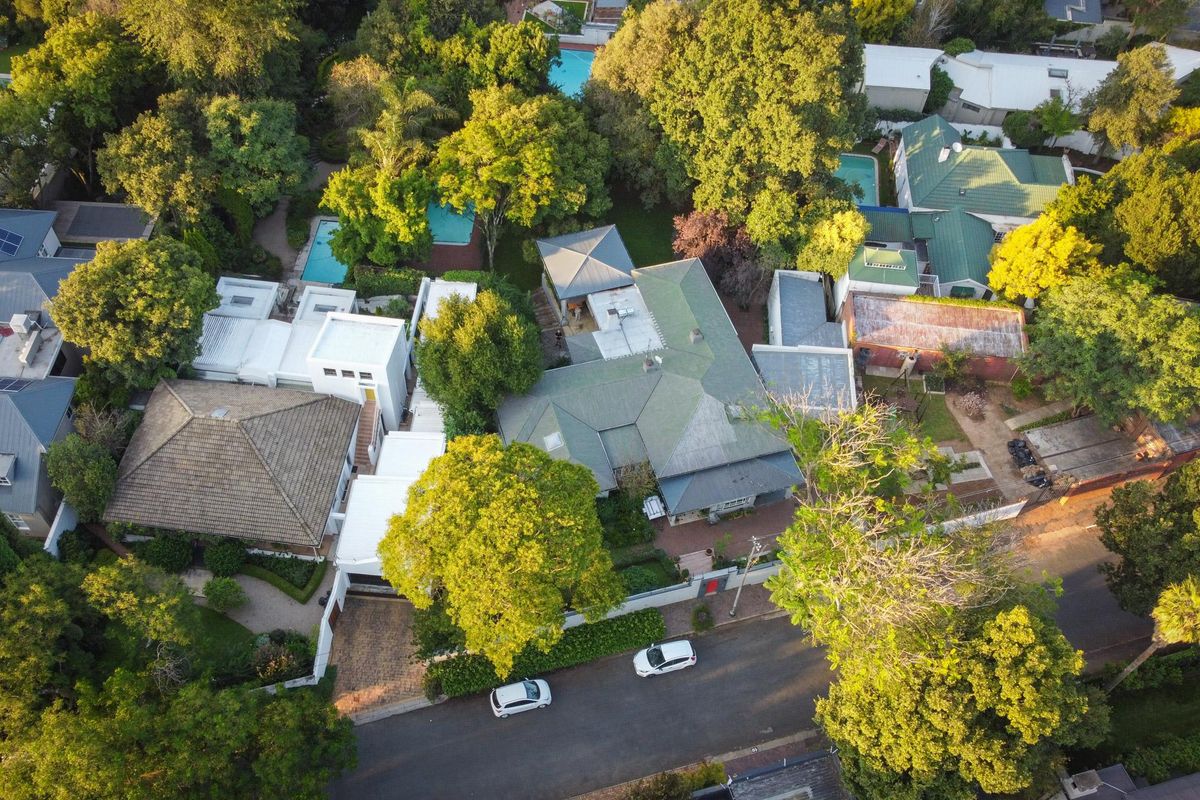 Aerial view of a residential property featuring multiple roof structures, mature trees, and swimming pools within a well-established neighborhood setting.