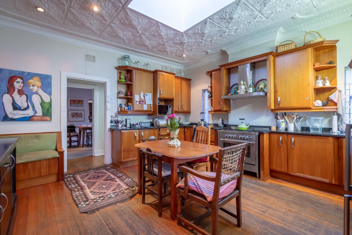 A spacious kitchen featuring timber cabinetry, granite countertops, a stainless steel range hood, and a decorative pressed metal ceiling with a central skylight.