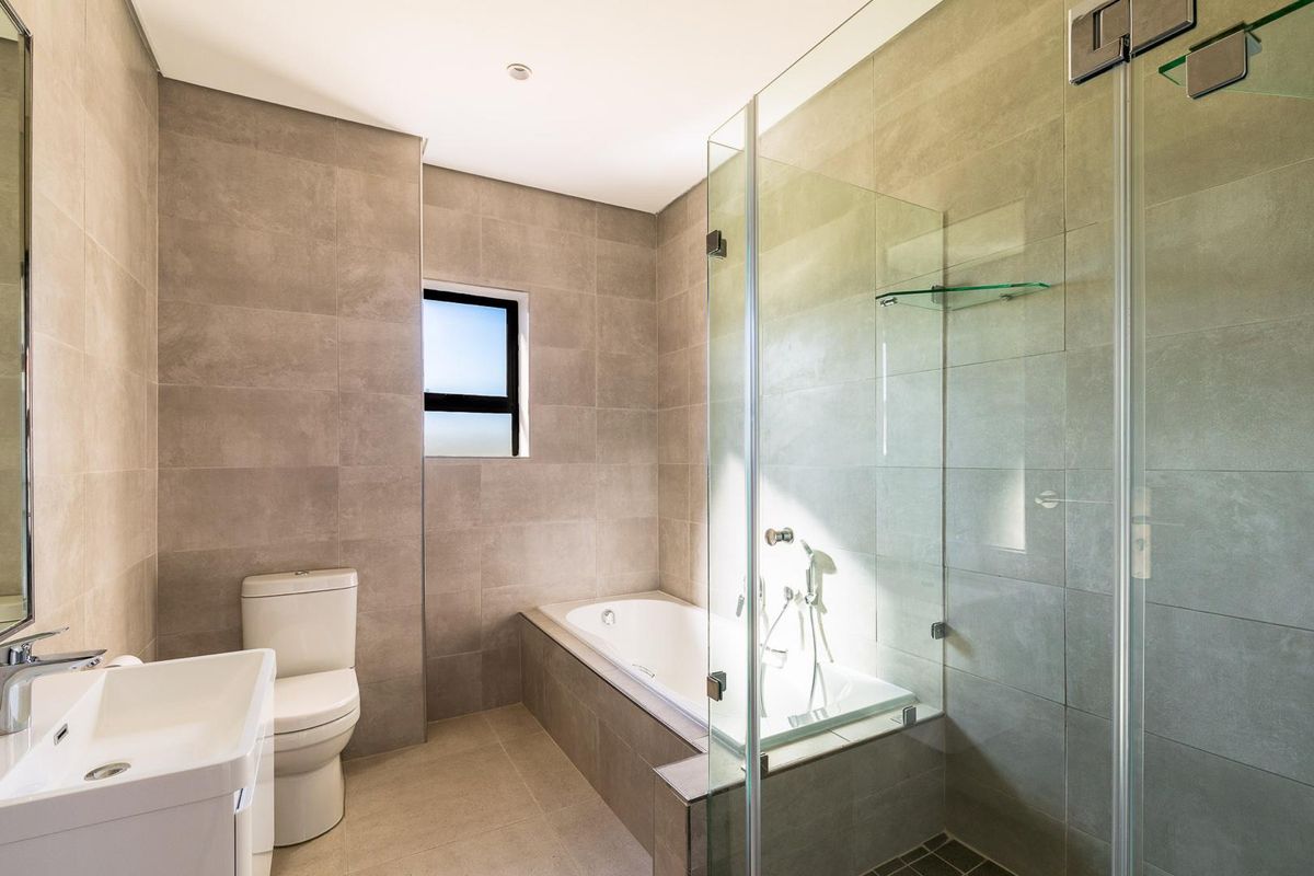 Modern bathroom featuring large format neutral wall tiles, a built-in bathtub, a glass-enclosed shower, and a contemporary vanity basin.