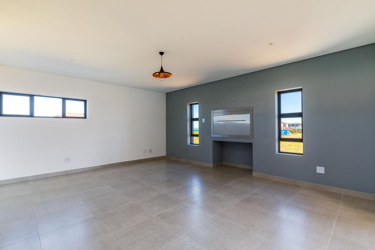 Spacious living area featuring large format floor tiles, a built-in fireplace, and modern aluminium-framed windows with neutral wall finishes.