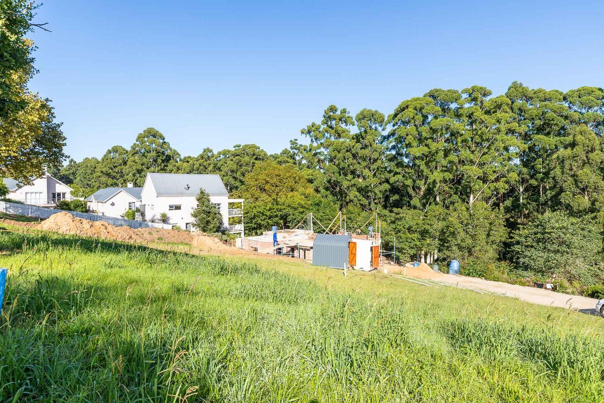 A view of a vacant residential plot currently under construction, featuring ongoing building works and surrounding established greenery.