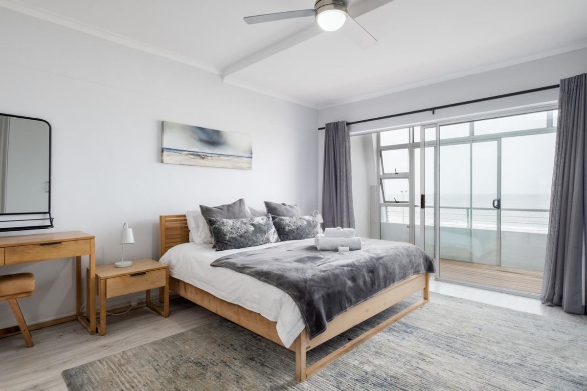 Bright bedroom featuring a ceiling fan, light wood-look flooring, and large sliding glass doors opening onto a private balcony with ocean views.