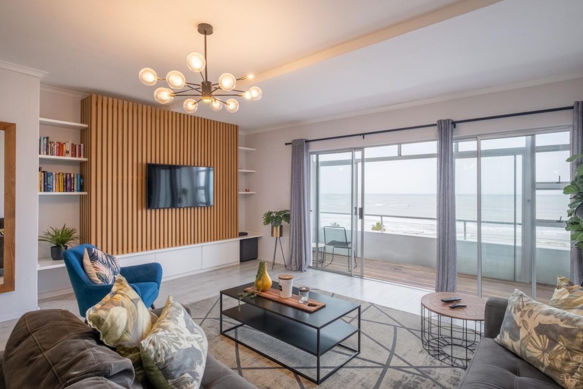 A bright living room featuring a modern slatted wood feature wall, built-in cabinetry, and large sliding glass doors opening onto a balcony with ocean views.