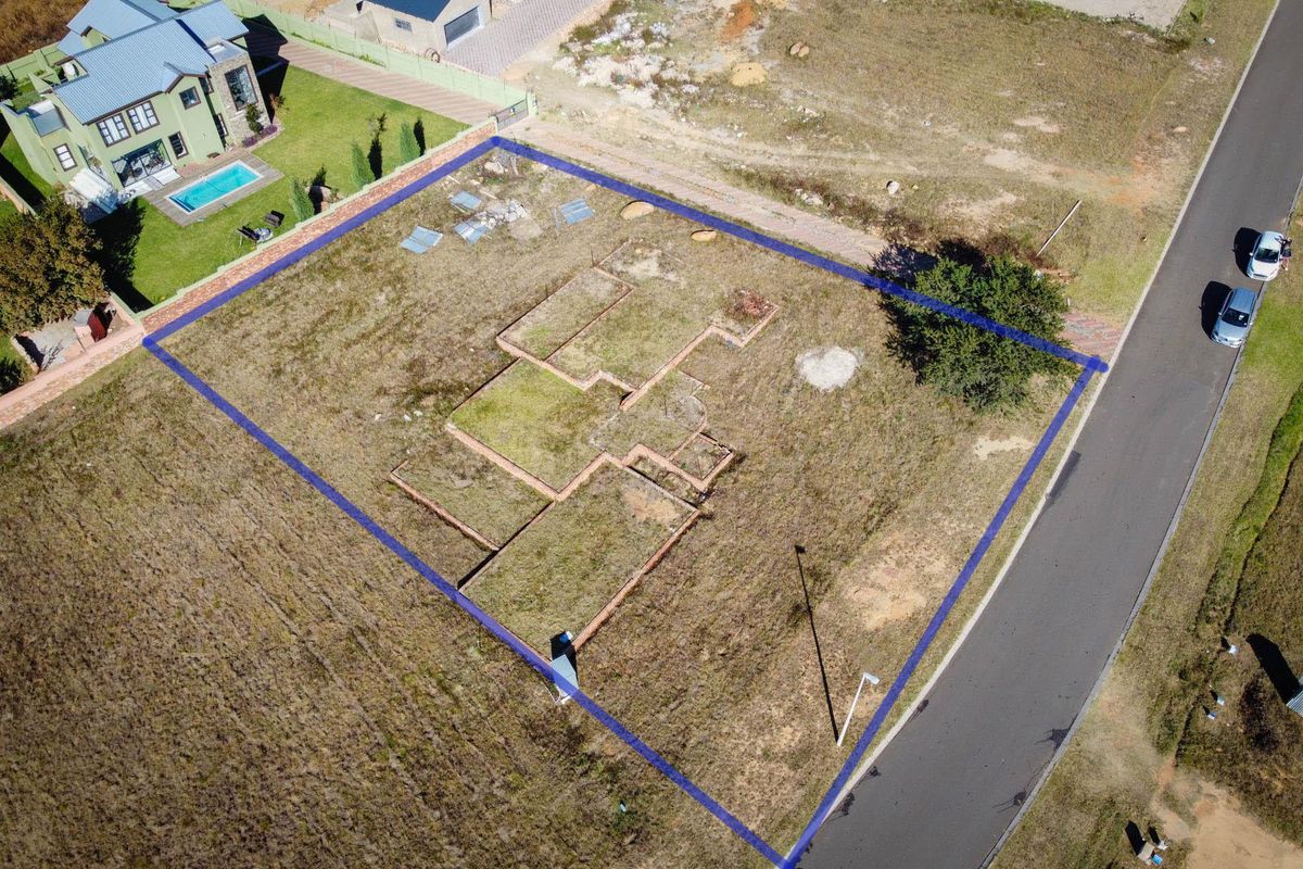 Aerial view of a vacant residential plot featuring exposed brick foundation footings and established grass, situated in a developed neighborhood.