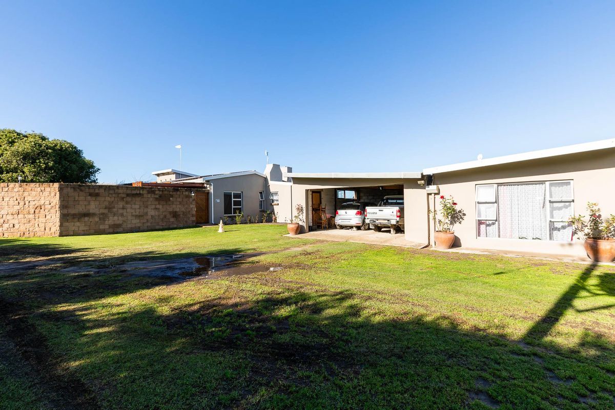 Rear view of the farm property featuring a spacious lawn, a covered carport area, and a perimeter boundary wall.