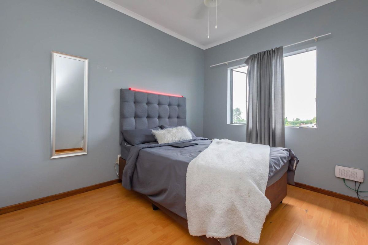 A bedroom featuring laminate flooring, a window with curtain rail, and a ceiling fan.
