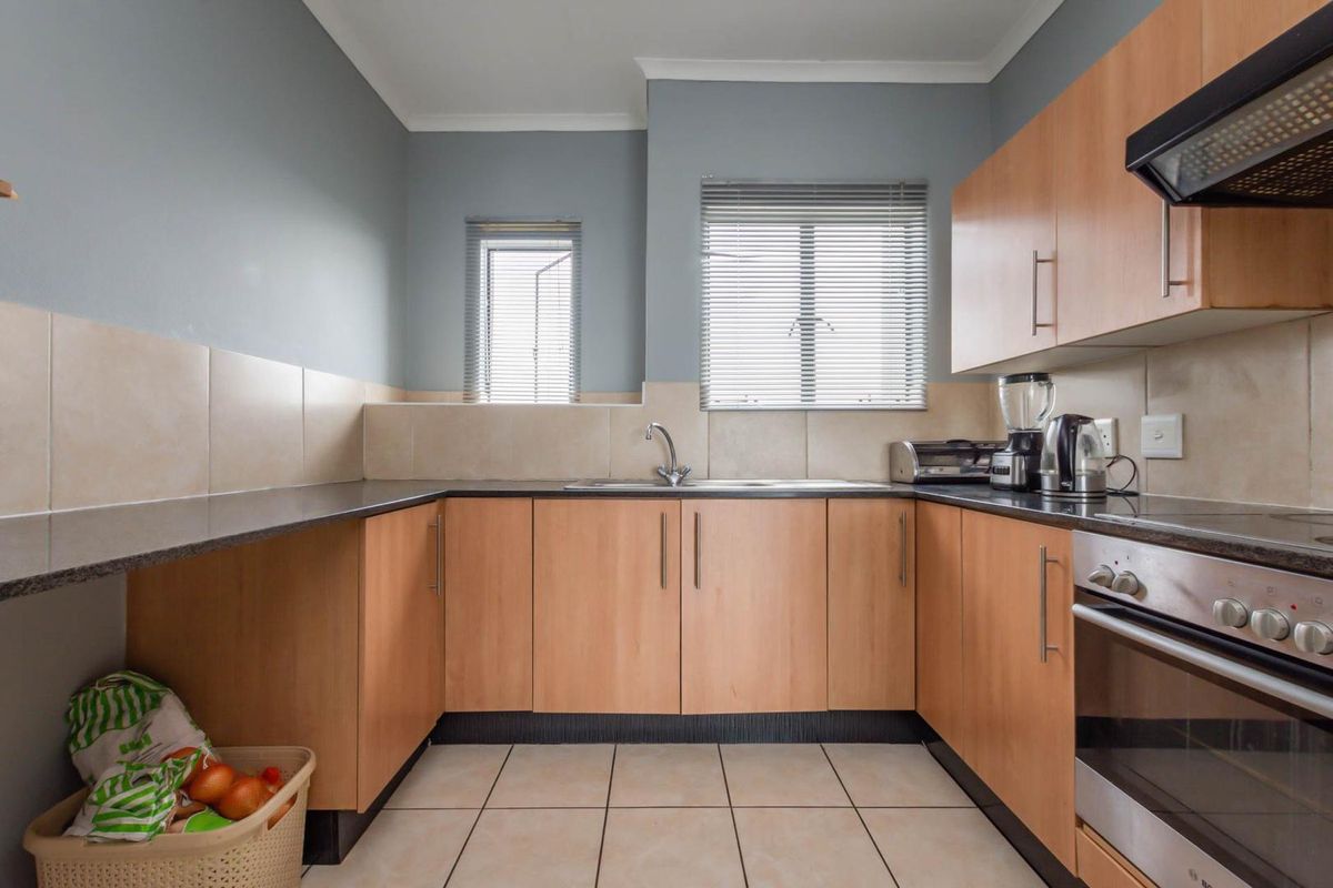 A functional U-shaped kitchen featuring light wood cabinetry, dark granite countertops, tiled splashbacks, and built-in oven with extractor fan.