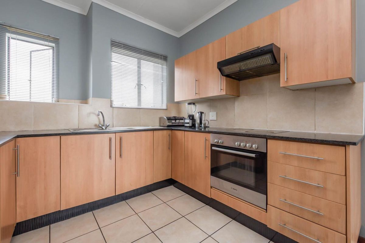 A functional kitchen featuring light wood cabinetry, dark granite countertops, tiled splashbacks, and a built-in oven with an extractor fan.