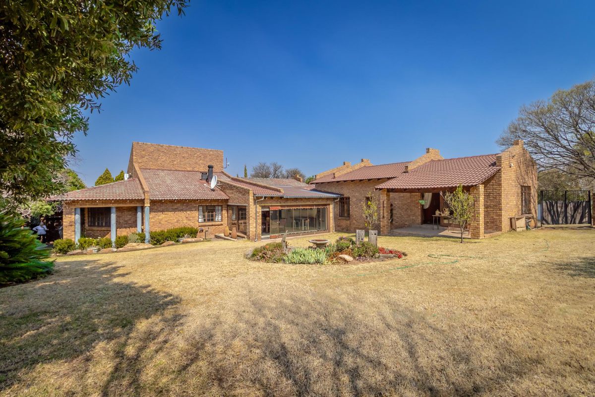 A spacious rear exterior view of a brick-built house featuring a tiled roof, covered patio area, and a large garden.