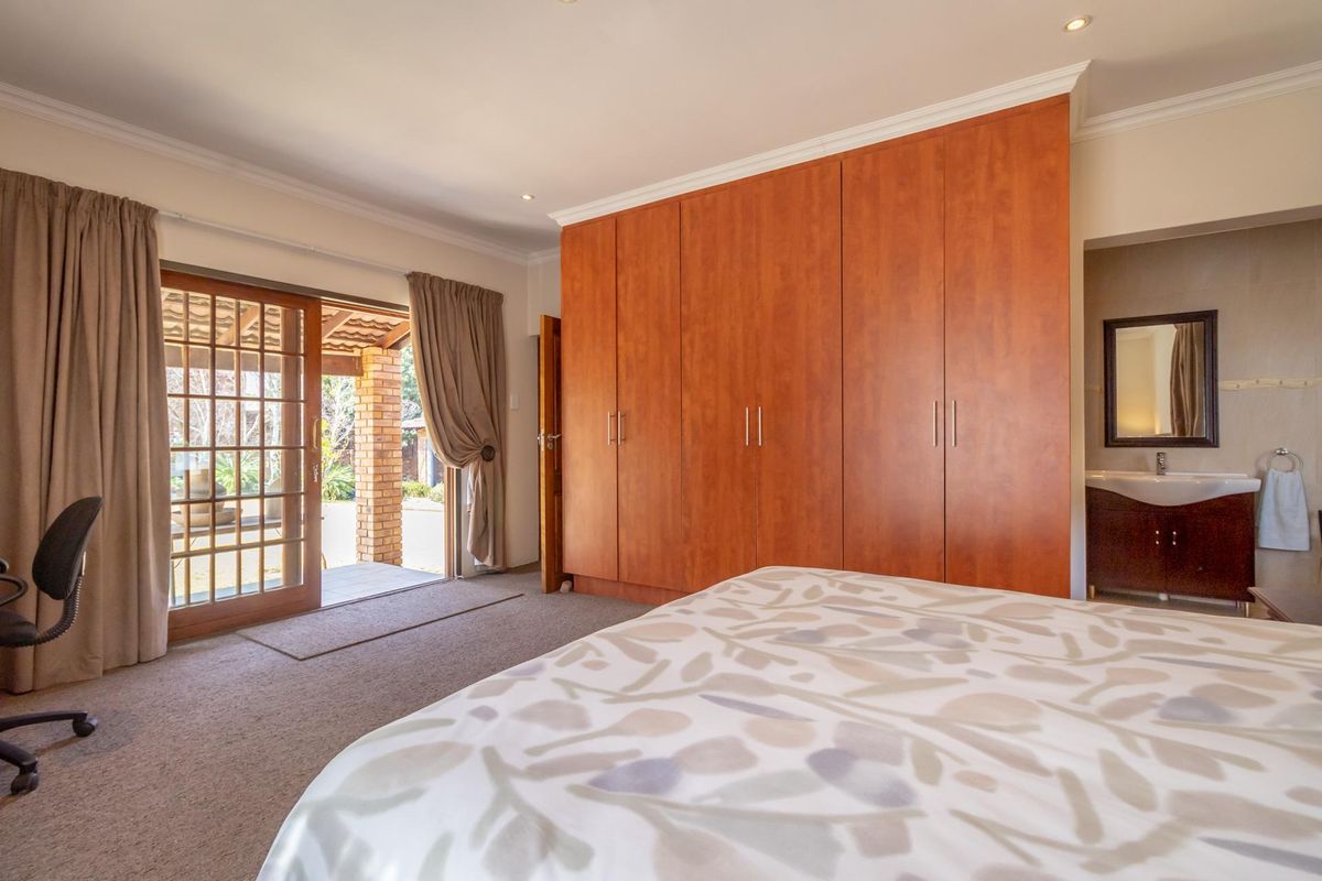 Spacious bedroom featuring built-in wooden cupboards, an en-suite vanity area, and sliding glass doors opening onto a covered patio.