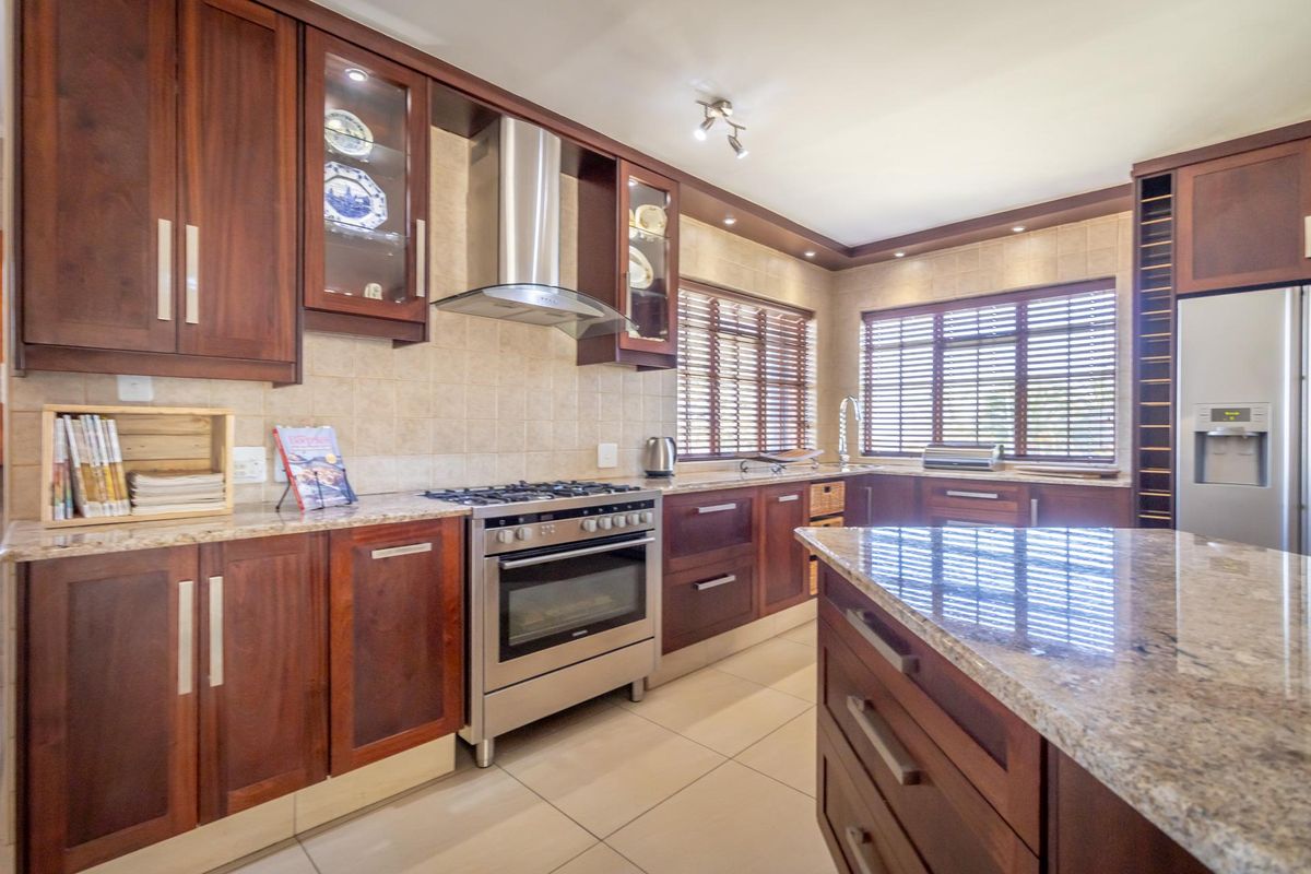 A well-appointed kitchen featuring dark wood cabinetry, granite countertops, a stainless steel gas stove with extractor fan, and a central island.