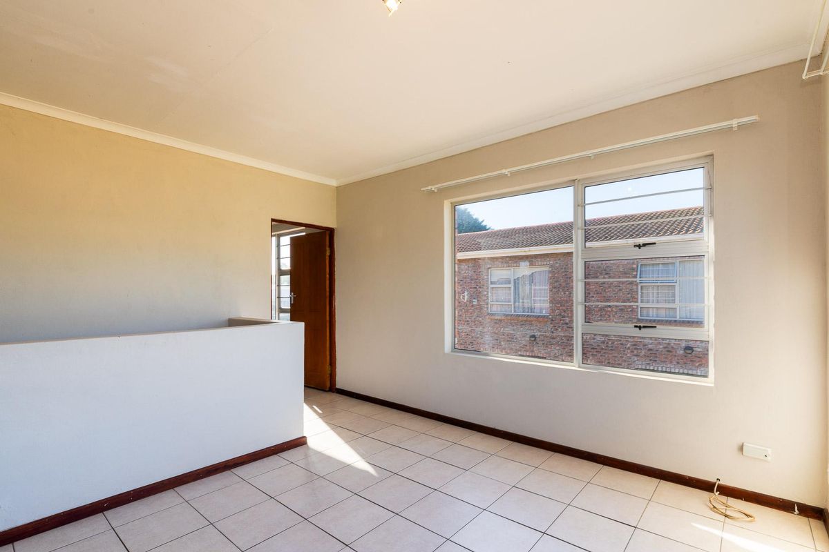 An empty bedroom featuring tiled flooring, a large window with security bars, and a low partition wall.