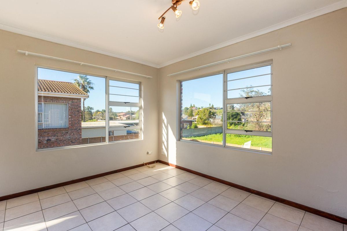 A bright, empty living area featuring large windows with neighborhood views, tiled flooring, and neutral wall finishes.