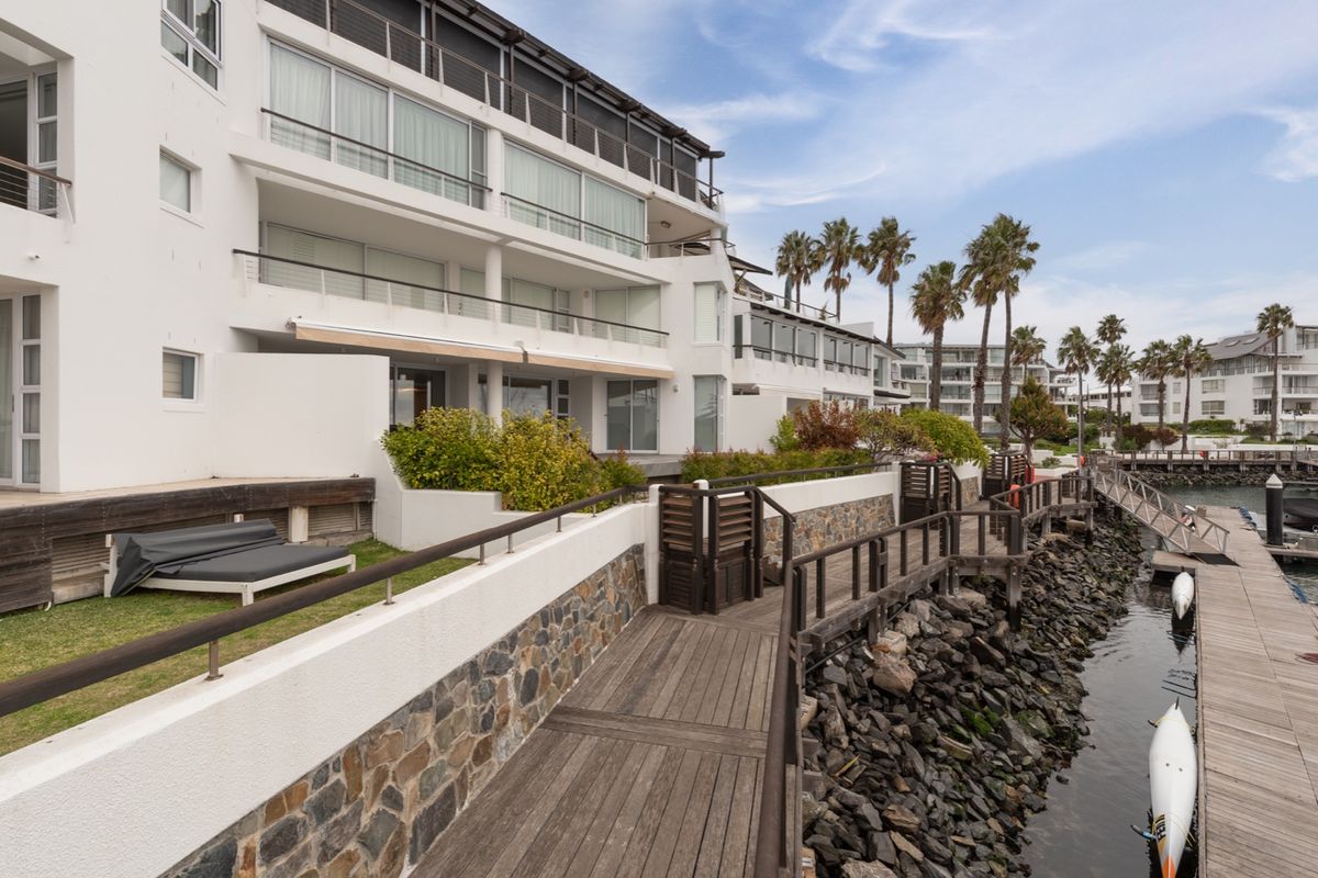 A view of the apartment complex exterior featuring a wooden boardwalk, stone retaining walls, and direct access to the waterfront.