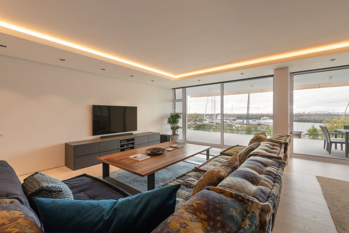 Modern living room featuring recessed cove lighting, large sliding glass doors, and direct access to a patio with marina views.