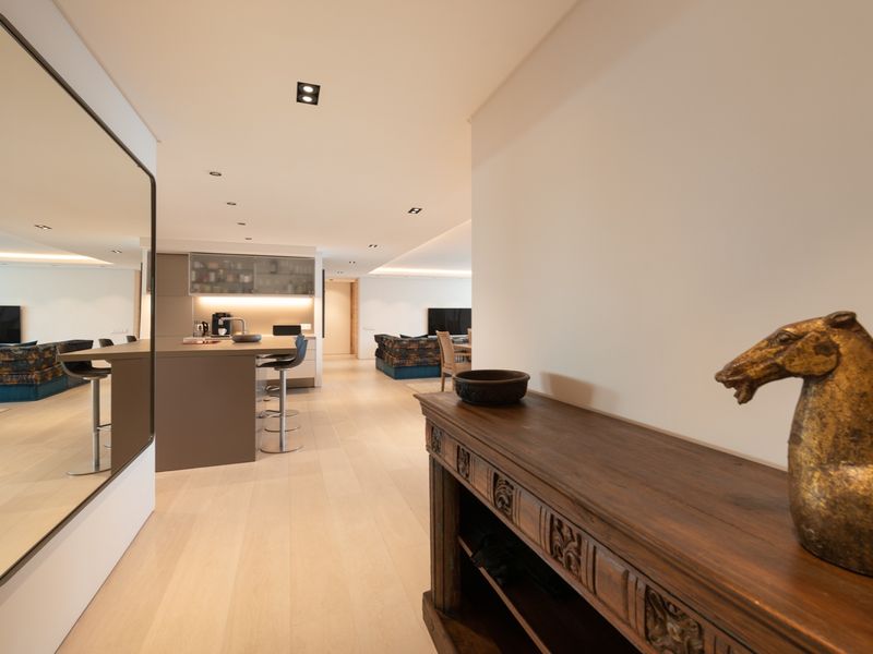 A modern open-plan living and kitchen area featuring light timber flooring, recessed ceiling lighting, and a sleek kitchen island with integrated cabinetry.