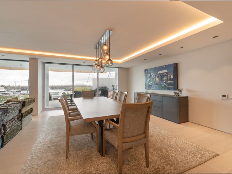 Spacious dining area featuring recessed ceiling lighting, modern tiled flooring, and large sliding glass doors opening to a balcony with marina views.