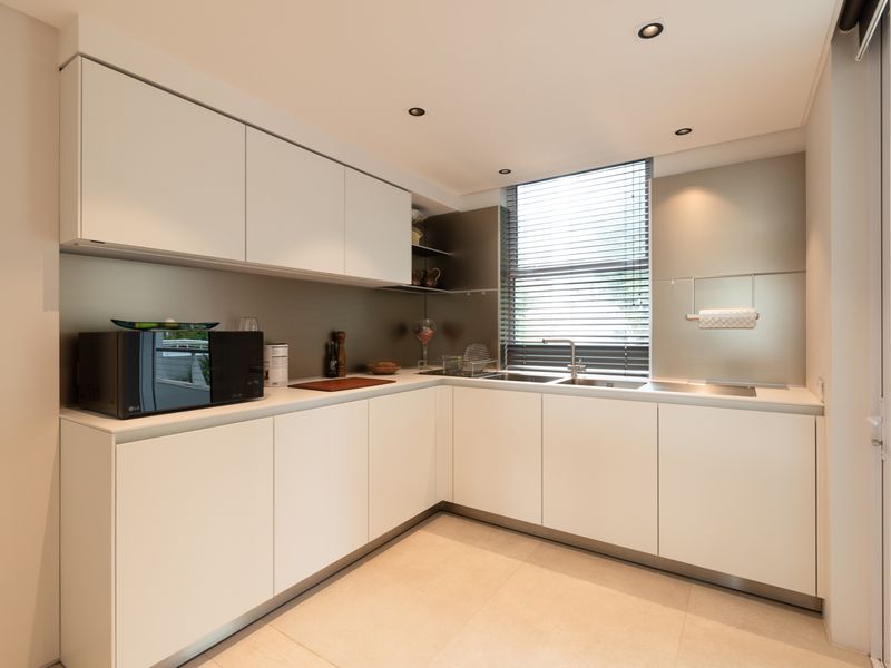 Modern kitchen featuring sleek white cabinetry, integrated stainless steel sink, metallic splashback, and recessed ceiling lighting.