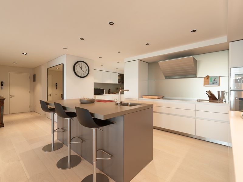 Modern open-plan kitchen featuring a central island with integrated sink, sleek cabinetry, built-in oven, and recessed ceiling lighting.