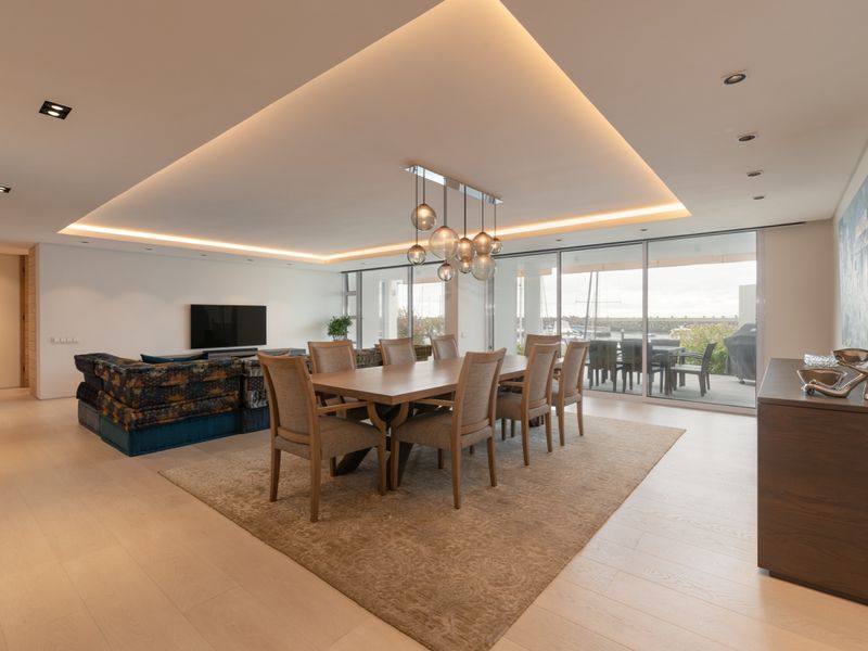 Spacious open-plan living and dining area featuring recessed tray ceiling lighting, light timber flooring, and large sliding glass doors leading to a private balcony.